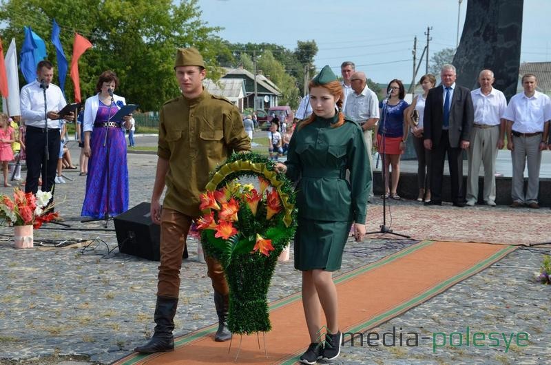 Корзину с цветами возлагают к братской могиле воинам, погибшим в годы Великой Отечественной войны