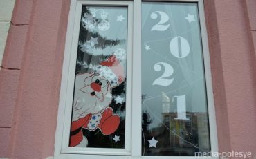 Бело-красно-белый дед Мороз выглядывает из окна учреждения, расположенного на центральной площади города