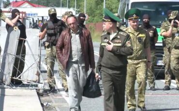 Дмитрий Смактунович в сопровождении беларусских пограничников идет к пункту пропуска «Брест». На заднем фоне вдоль линии госграницы стоят польские пограничники. 12 июня 2024 года. Скриншот видео